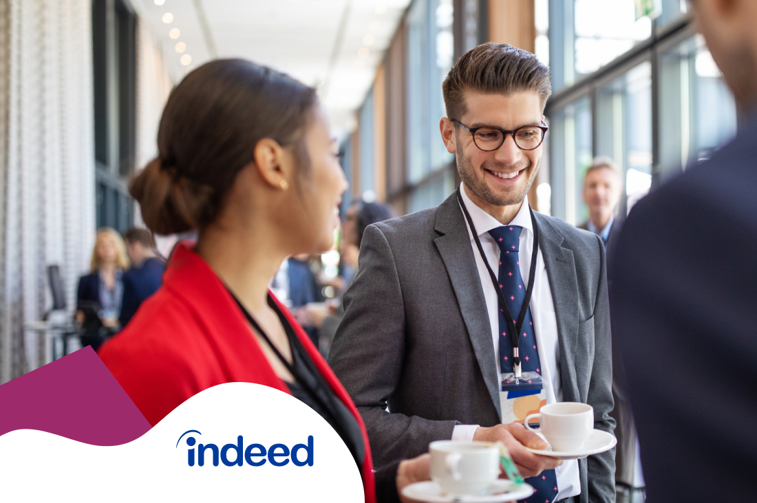 A man and a woman smiling and holding a cup of hot drink during a conference networking session