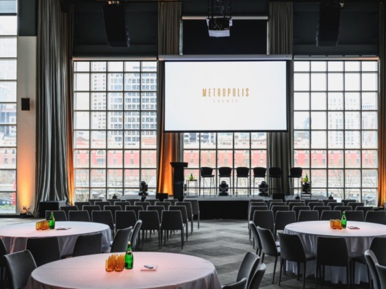 Conference venue with tall windows, projector, and circular tables.