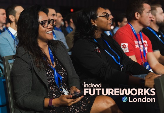 A group of people is sitting to listen to a speaker, they are attentive and smiling. The logo "Indeed FutureWorks London" is added to the image.