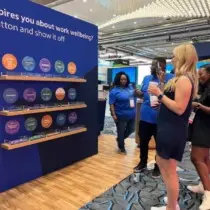 A woman is smiling while taking a photo of shelves showcasing work wellbeing keywords