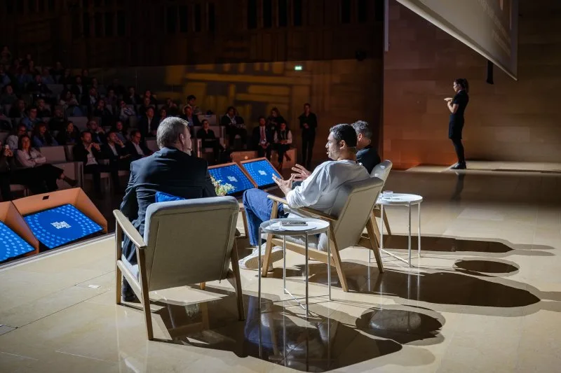 Des orateurs assis sur scène lors d'un grand événement, présentant devant un public