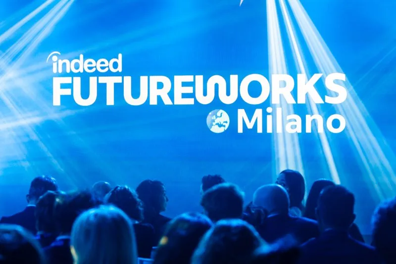 Una grande folla osserva un palco illuminato di blu durante un evento.