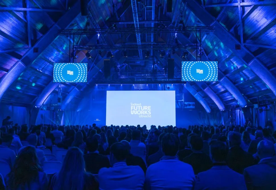 Een grote menigte kijkt naar een blauw verlicht podium tijdens een evenement.