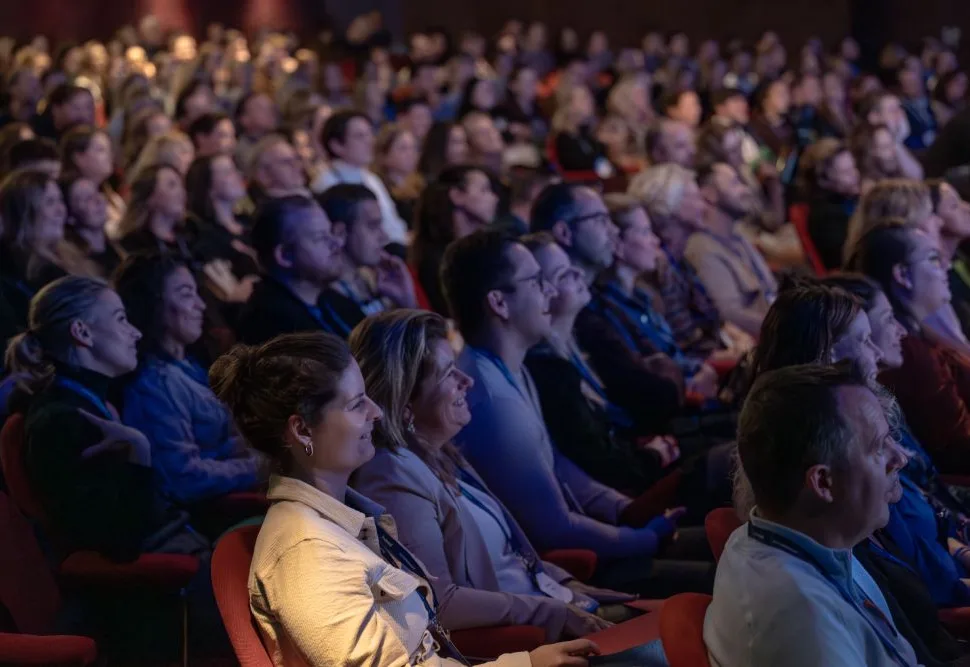 Een groot publiek luistert naar een spreker tijdens een evenement.