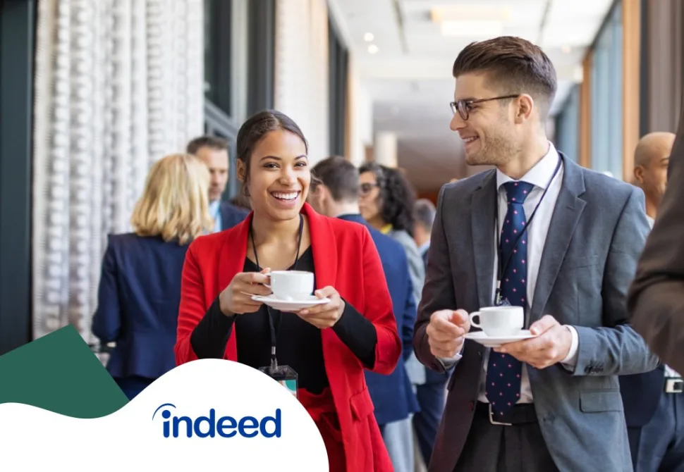 Two well dressed event-goers smiling and chatting while drinking coffee at an event